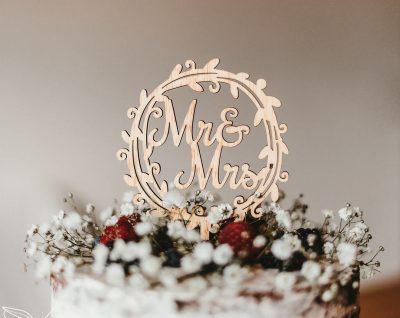 Un gâteau de mariage garni de fleurs blanches, de baies et d'un panneau en bois sur lequel est écrit M. et Mme à l'intérieur d'un cadre circulaire décoratif.